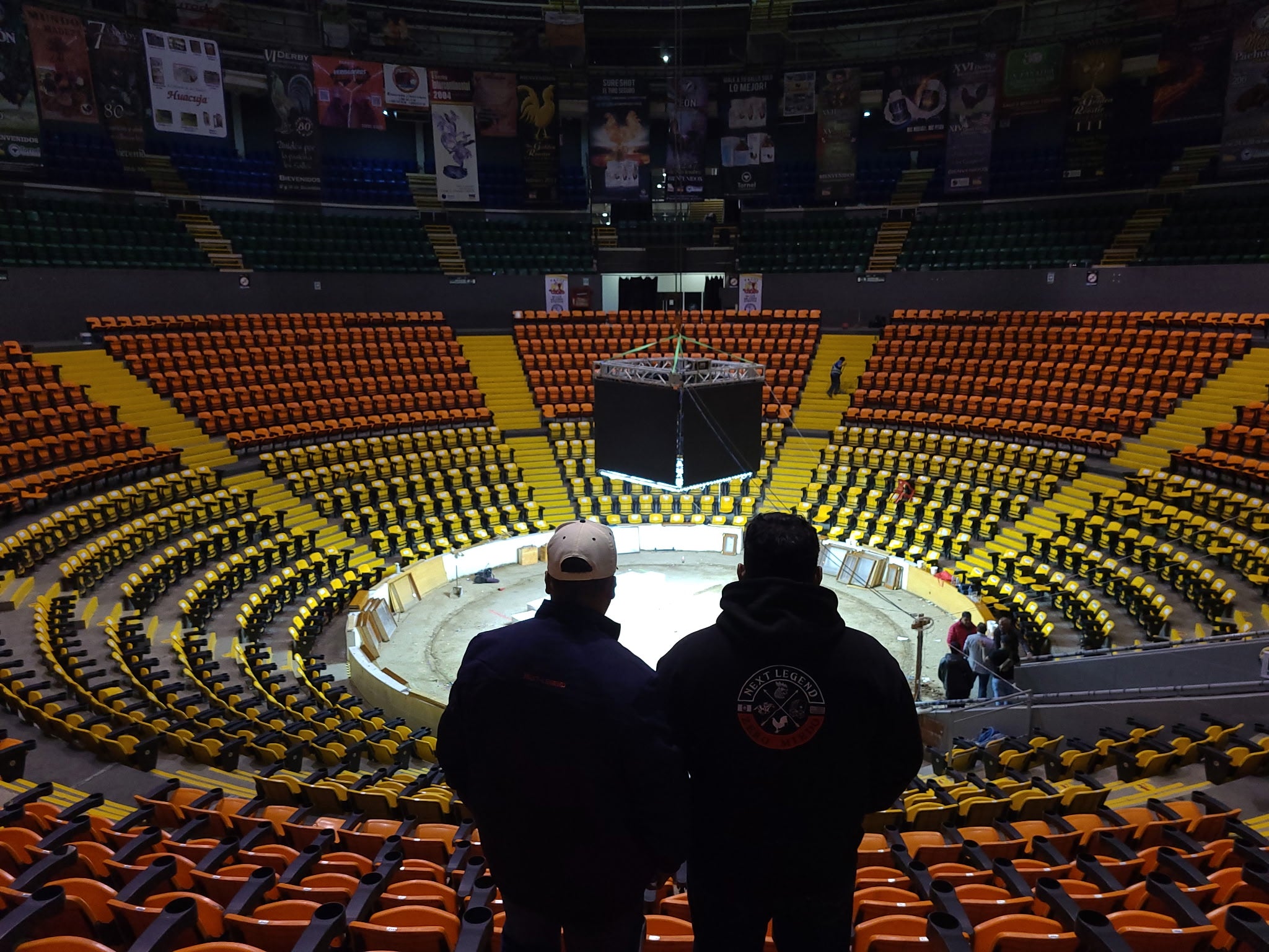 Two people standing in an empty arena with orange and yellow seats.